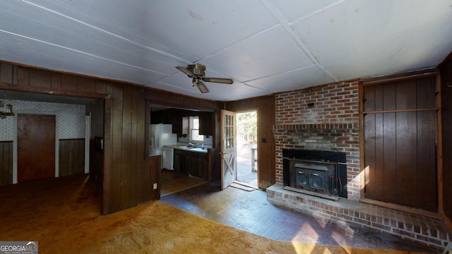 unfurnished living room with ceiling fan, carpet, wood walls, and a brick fireplace