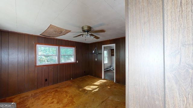 carpeted spare room with ceiling fan, a baseboard heating unit, and wooden walls