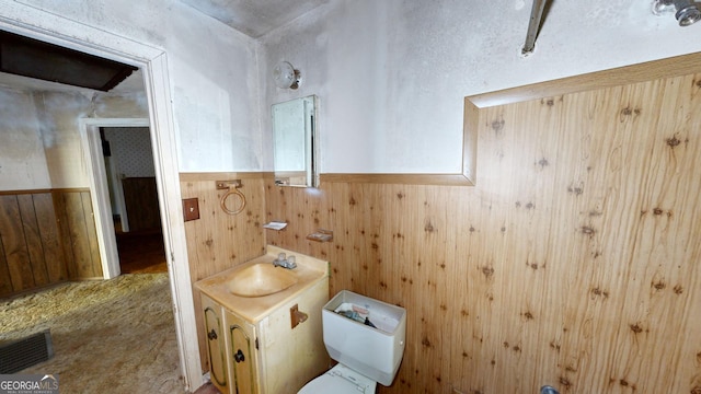 bathroom featuring toilet, vanity, and wooden walls