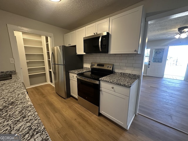 kitchen with dark stone countertops, hardwood / wood-style flooring, appliances with stainless steel finishes, a textured ceiling, and white cabinets