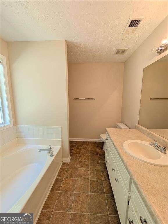 bathroom with a textured ceiling, toilet, vanity, and a bath