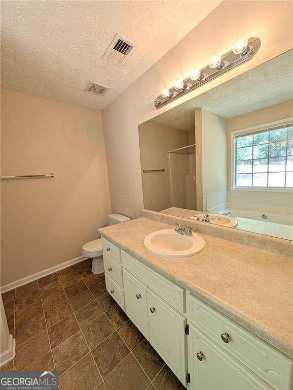 bathroom featuring toilet, vanity, walk in shower, and a textured ceiling