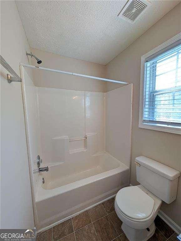 bathroom featuring tub / shower combination, a textured ceiling, and toilet