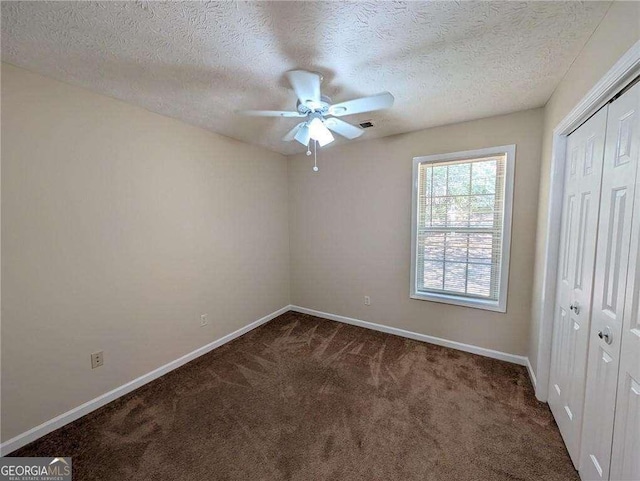 unfurnished bedroom featuring a textured ceiling, ceiling fan, a closet, and dark carpet