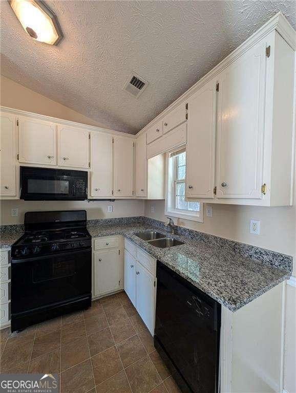 kitchen featuring white cabinets, black appliances, sink, vaulted ceiling, and light stone counters