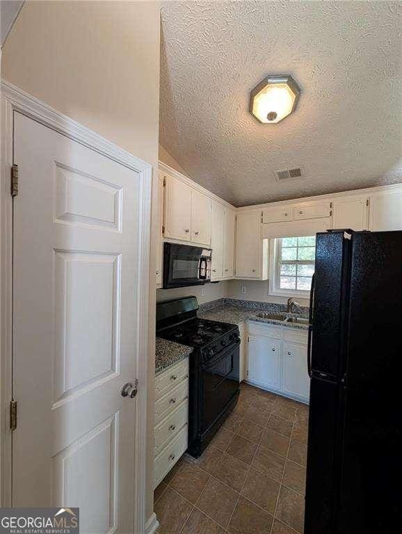 kitchen with vaulted ceiling, black appliances, white cabinetry, a textured ceiling, and dark stone counters