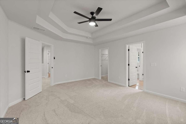 unfurnished bedroom with a spacious closet, ceiling fan, a closet, and a tray ceiling