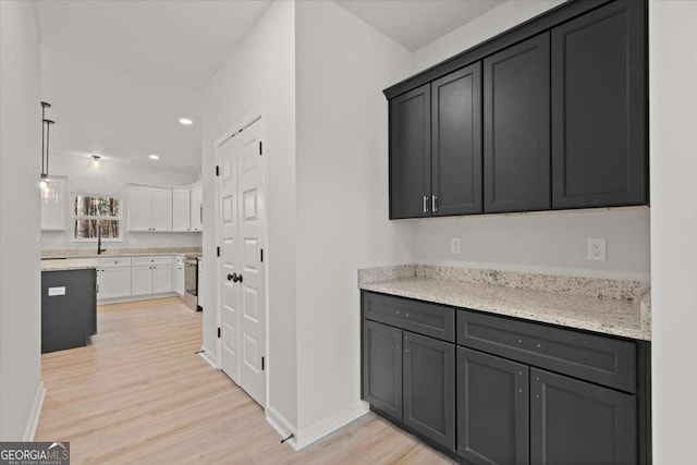 kitchen with stainless steel range with electric cooktop, white cabinetry, light hardwood / wood-style floors, and light stone counters