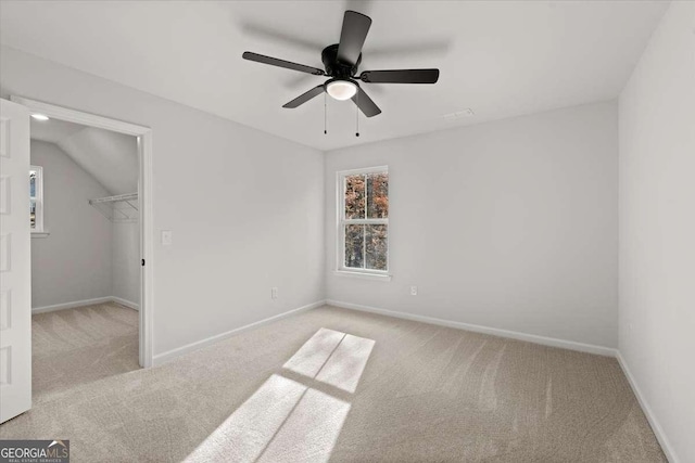 unfurnished bedroom featuring a spacious closet, light carpet, a closet, vaulted ceiling, and ceiling fan