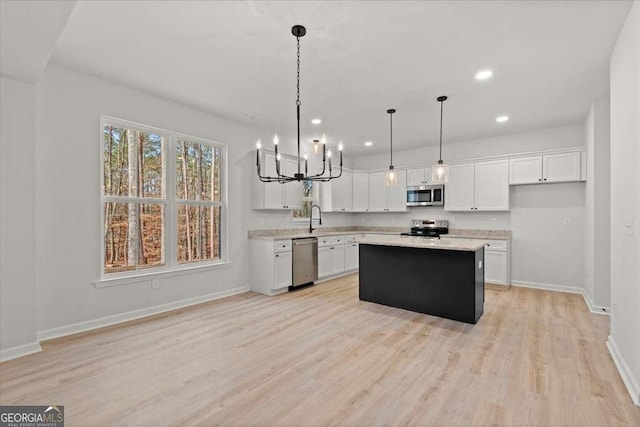 kitchen with a center island, white cabinetry, hanging light fixtures, light wood-type flooring, and stainless steel appliances