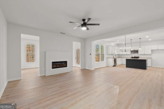 unfurnished living room featuring ceiling fan, sink, and light wood-type flooring