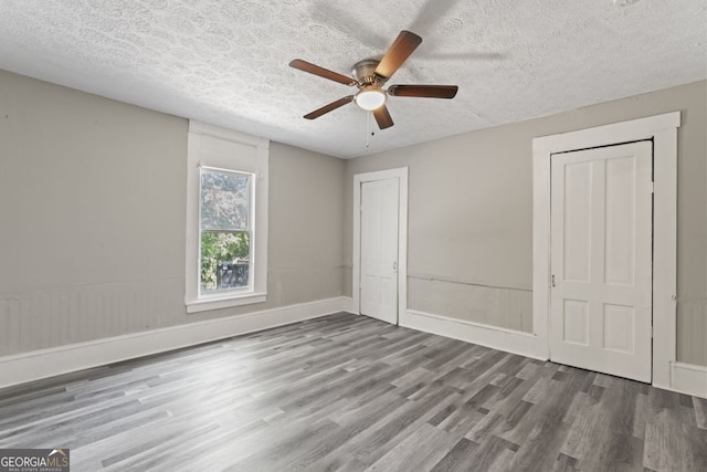 unfurnished bedroom featuring wood-type flooring, two closets, ceiling fan, and a textured ceiling