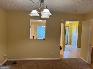 carpeted empty room featuring a textured ceiling and a notable chandelier