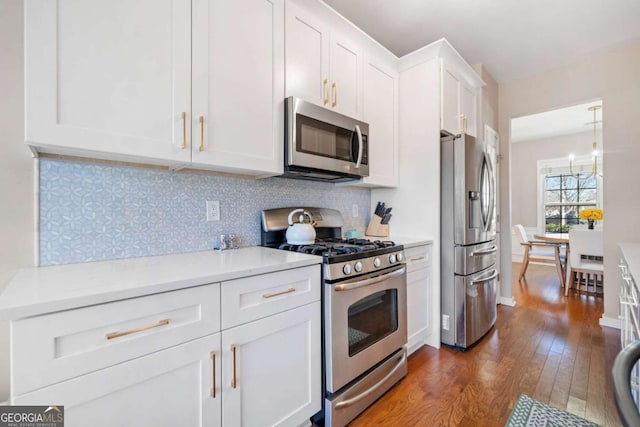 kitchen with white cabinets, appliances with stainless steel finishes, dark wood-type flooring, tasteful backsplash, and hanging light fixtures