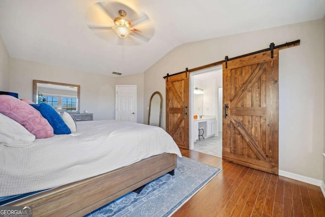 bedroom featuring ceiling fan, a barn door, vaulted ceiling, hardwood / wood-style flooring, and connected bathroom