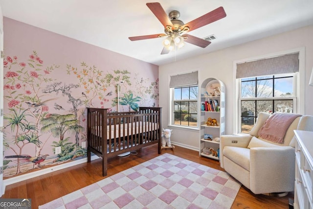 bedroom with ceiling fan, hardwood / wood-style floors, and a crib