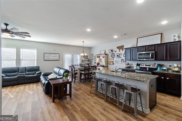 kitchen featuring appliances with stainless steel finishes, a kitchen bar, an island with sink, hanging light fixtures, and light stone counters