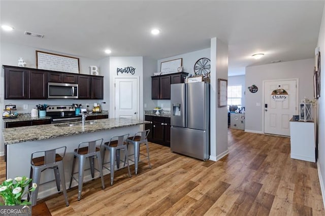 kitchen with appliances with stainless steel finishes, an island with sink, sink, dark brown cabinets, and a breakfast bar area