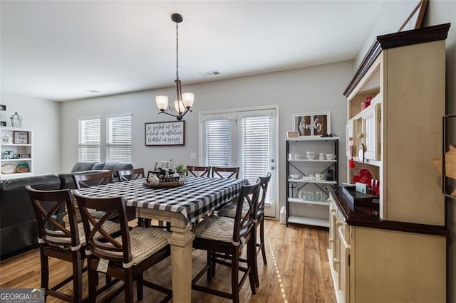 dining space featuring light wood-type flooring, a healthy amount of sunlight, and a notable chandelier