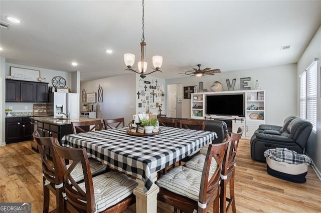 dining area featuring light wood-type flooring, sink, and ceiling fan with notable chandelier