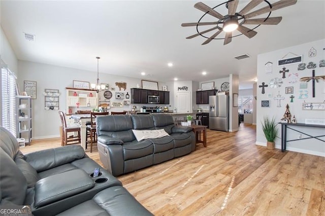 living room featuring ceiling fan with notable chandelier and light hardwood / wood-style floors