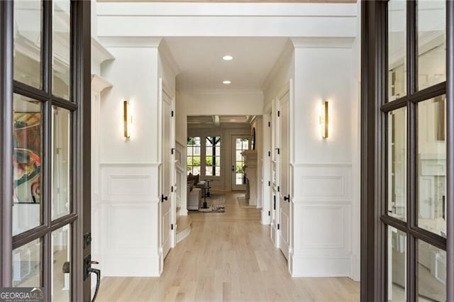 hallway featuring light hardwood / wood-style floors, ornamental molding, and french doors