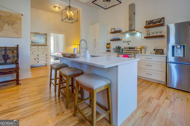 kitchen with exhaust hood, white cabinetry, appliances with stainless steel finishes, a kitchen island with sink, and hanging light fixtures