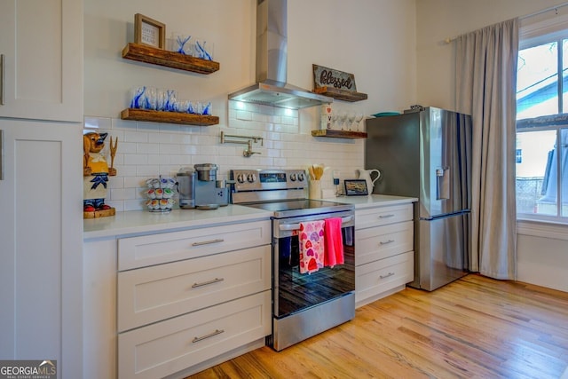 kitchen with wall chimney range hood, decorative backsplash, light hardwood / wood-style flooring, appliances with stainless steel finishes, and white cabinets