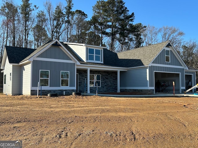 view of front facade with board and batten siding, a porch, roof with shingles, a garage, and stone siding