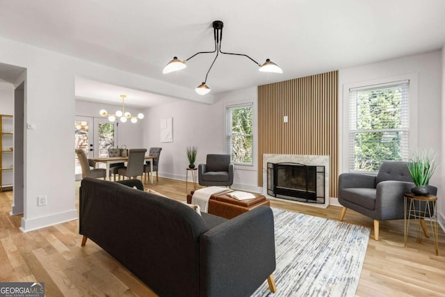 living room with a wealth of natural light, a notable chandelier, a premium fireplace, and light wood-type flooring