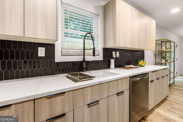 kitchen with light wood-type flooring, light brown cabinetry, light stone countertops, stainless steel dishwasher, and sink