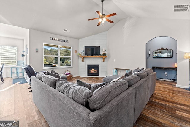 living room featuring dark wood-type flooring, ceiling fan, a fireplace, and vaulted ceiling