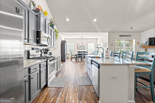 kitchen with light stone countertops, stainless steel appliances, an island with sink, a breakfast bar, and gray cabinetry