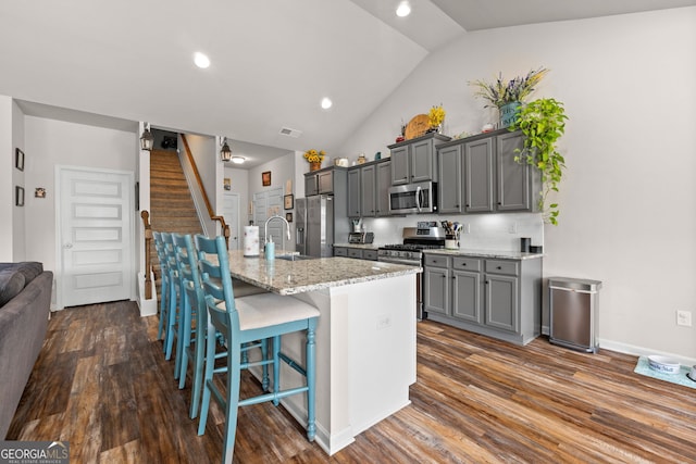 kitchen with a center island with sink, appliances with stainless steel finishes, gray cabinetry, a kitchen breakfast bar, and sink