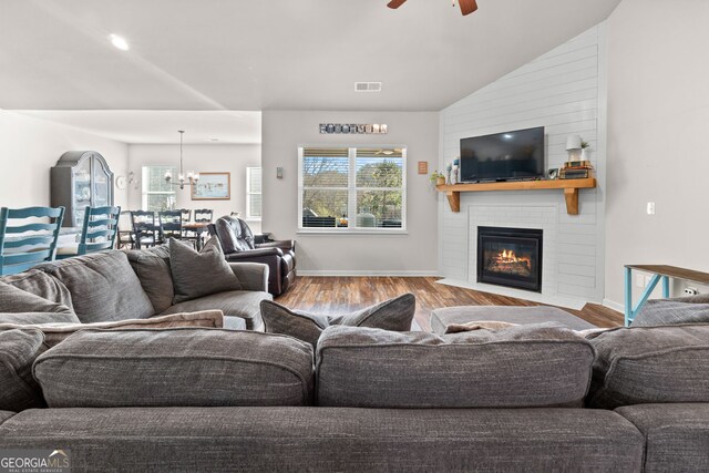 living room with light hardwood / wood-style flooring, ceiling fan with notable chandelier, a fireplace, and plenty of natural light