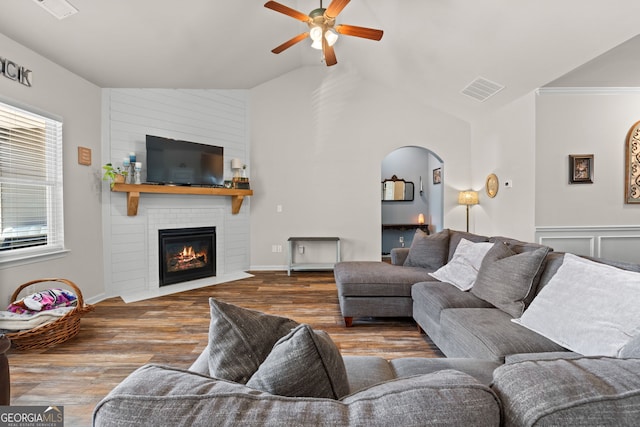 living room featuring lofted ceiling, a fireplace, dark hardwood / wood-style floors, ornamental molding, and ceiling fan