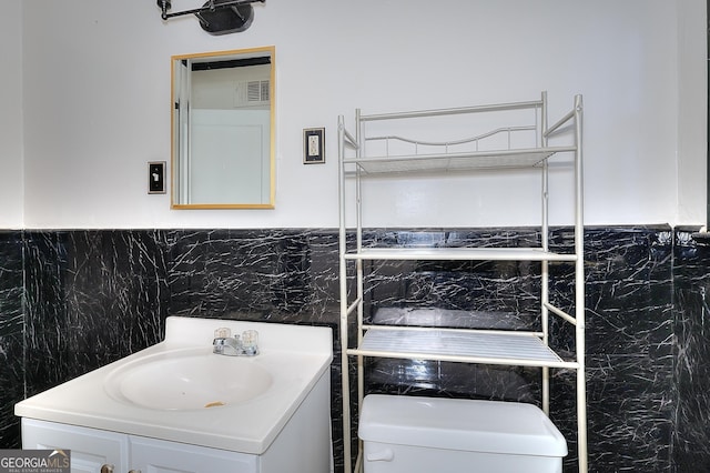 bathroom featuring toilet, vanity, and tile walls