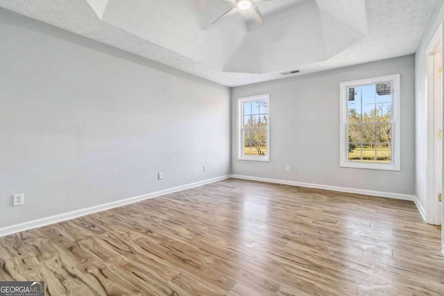 empty room with a raised ceiling, light wood-type flooring, plenty of natural light, and ceiling fan