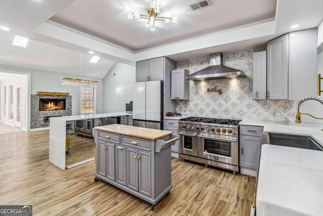 kitchen featuring tasteful backsplash, gray cabinets, fridge, range with two ovens, and wall chimney exhaust hood