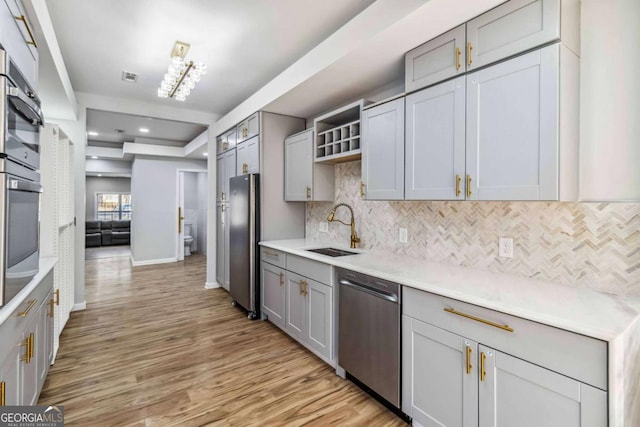 kitchen featuring backsplash, light hardwood / wood-style floors, sink, appliances with stainless steel finishes, and gray cabinetry