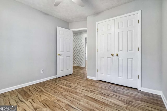 unfurnished bedroom with ceiling fan, a textured ceiling, a closet, and light wood-type flooring