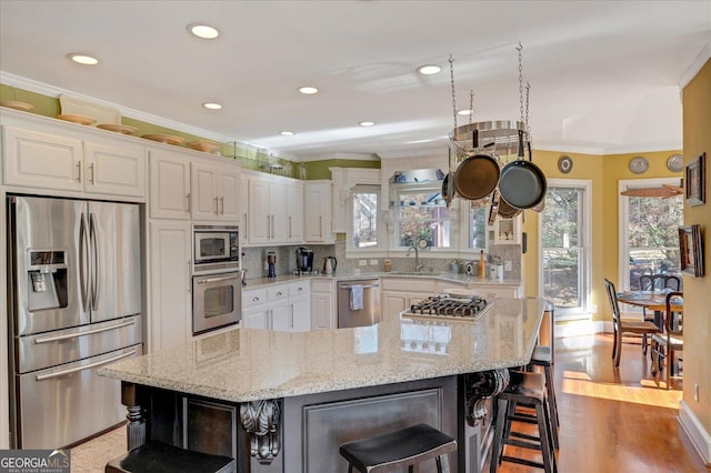 kitchen with white cabinets, appliances with stainless steel finishes, a center island, a kitchen bar, and light stone counters