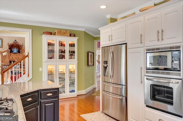 kitchen featuring white cabinetry, light hardwood / wood-style flooring, appliances with stainless steel finishes, ornamental molding, and light stone counters