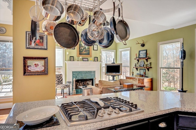 kitchen with light stone countertops, stainless steel gas stovetop, ornamental molding, and a premium fireplace