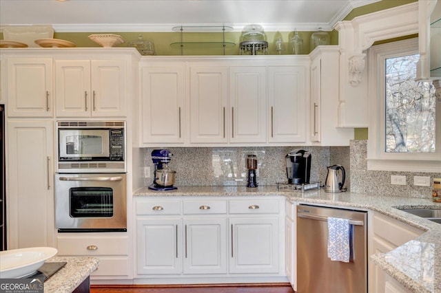 kitchen featuring white cabinets, stainless steel appliances, backsplash, light stone counters, and crown molding