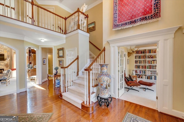 staircase featuring ornamental molding, wood-type flooring, built in features, and a high ceiling