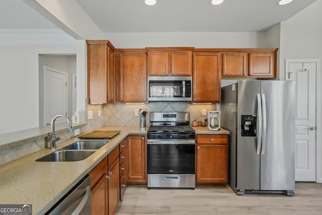 kitchen featuring stainless steel appliances, sink, backsplash, light wood-type flooring, and light stone counters