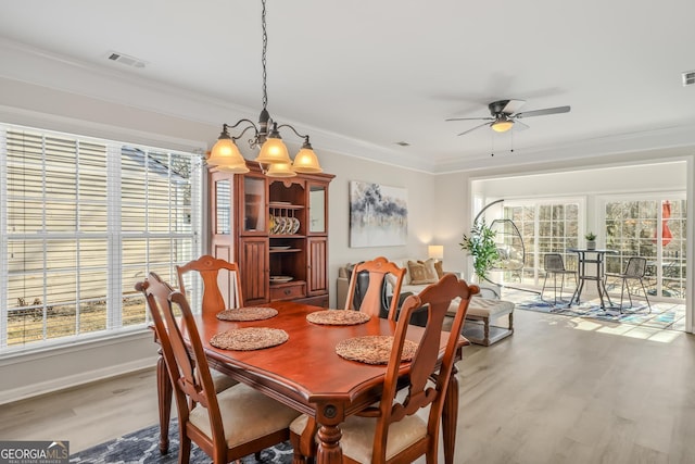 dining area featuring ceiling fan with notable chandelier, wood-type flooring, and crown molding