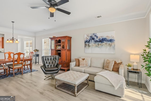 living room with ceiling fan with notable chandelier, ornamental molding, and light wood-type flooring