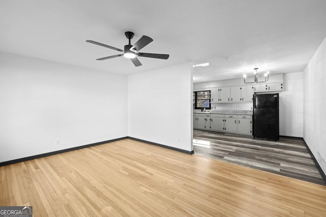 unfurnished living room featuring ceiling fan with notable chandelier and hardwood / wood-style flooring